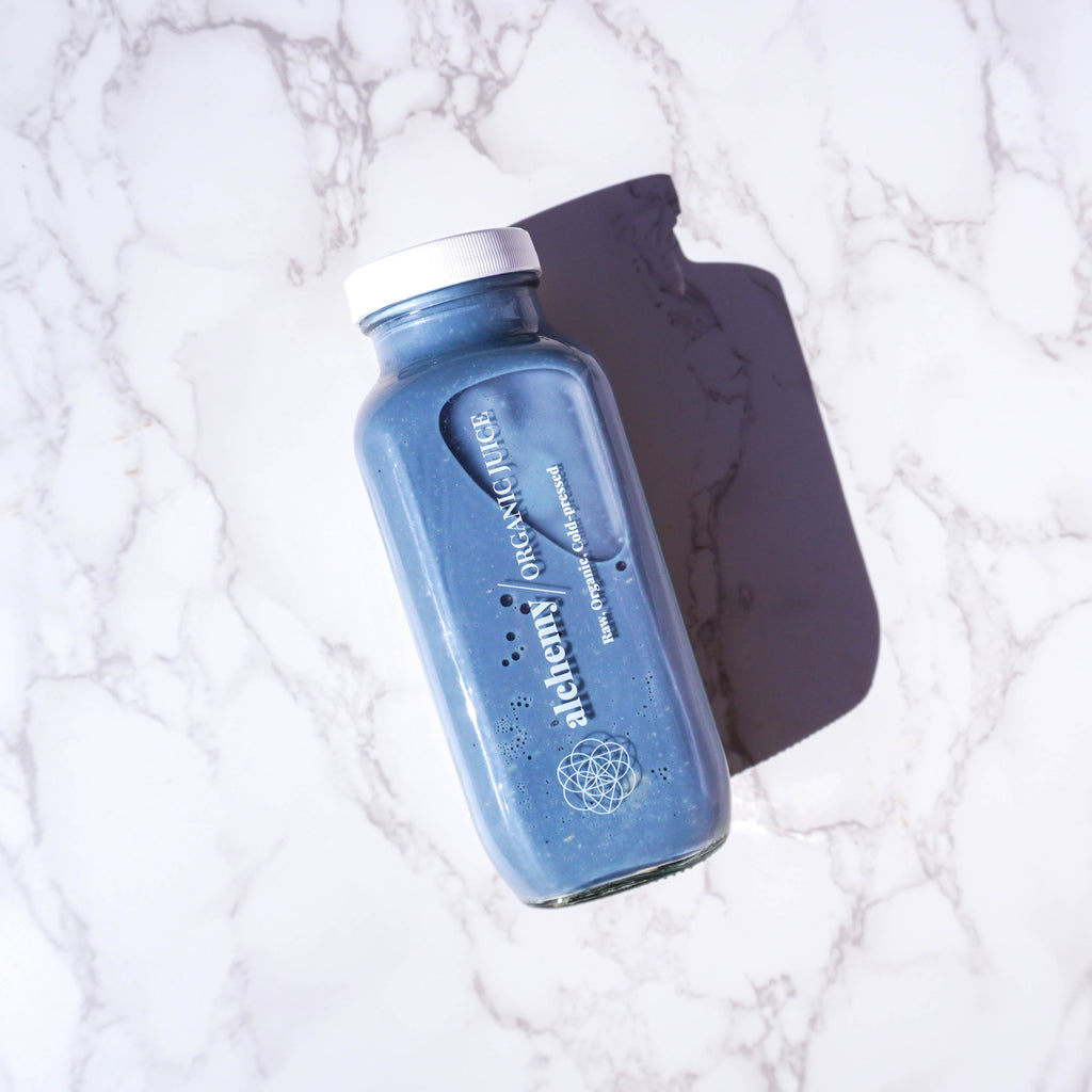 A bottle of Alchemy Organics' Blue Cosmic Peppermint Latte placed on a marble surface, showcasing its vibrant blue color and exclusive branding.